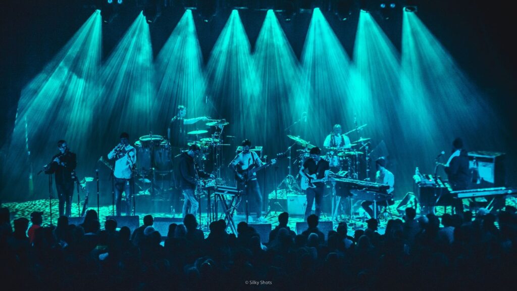 Snarky Puppy tocando en el escenario mientras el público disfruta de la música y unas luces azules crean un ambiente mágico