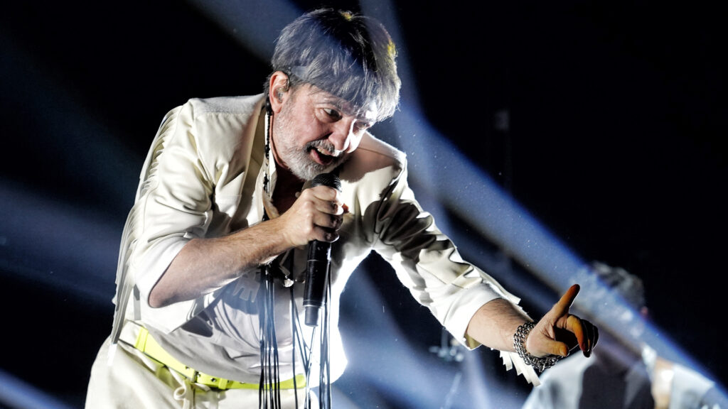 Adrián Dárgelos, vocalista de Babasónicos, interpretando una canción en vivo con su icónico gesto de hacer un número uno con su mano mientras sostiene un micrófono en la otra