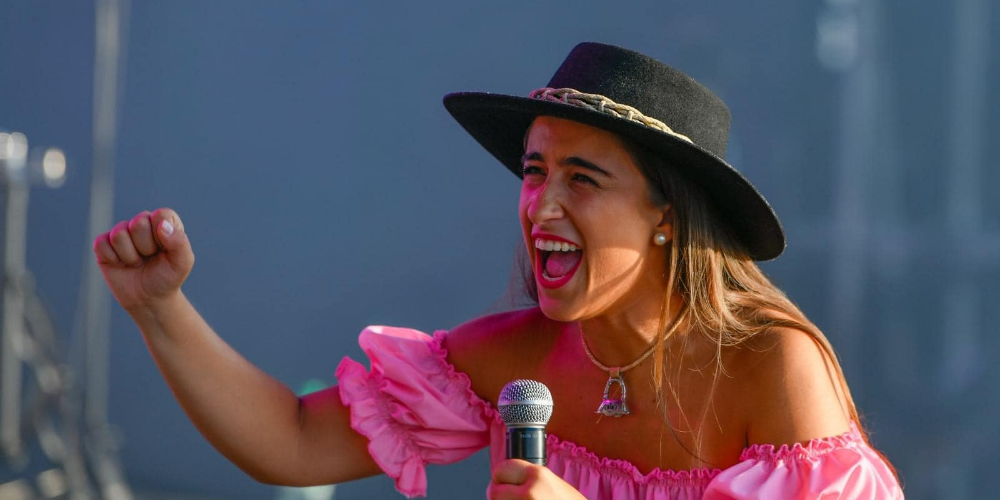 Catherine Vergnes vestida de rosa con sombrero negro y micrófono en mano