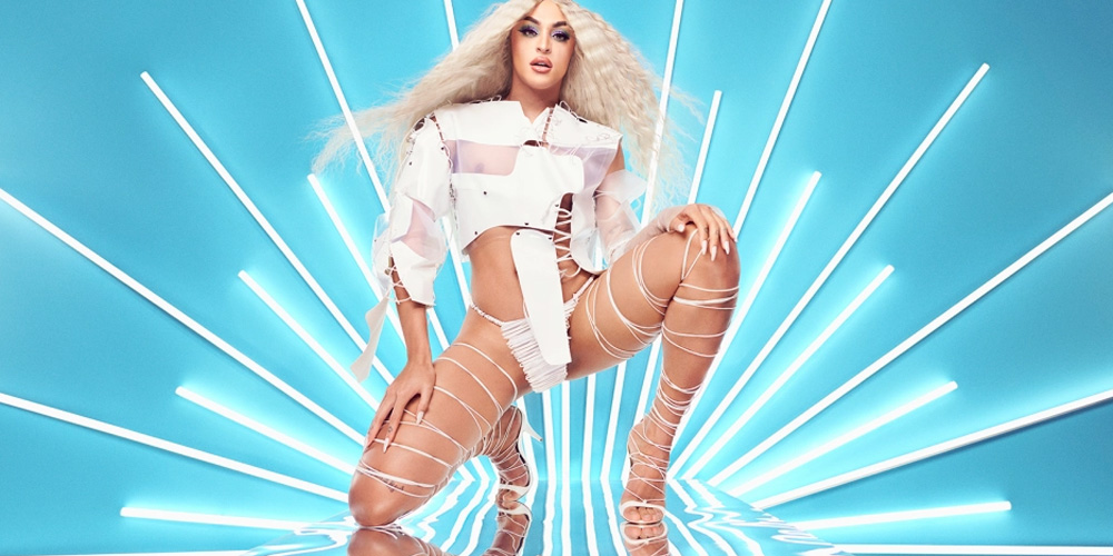 Imagen de Pabllo Vittar posando con un atuendo descubierto de tiras blancas, con pelo suelto y fondo azul con luces blancas