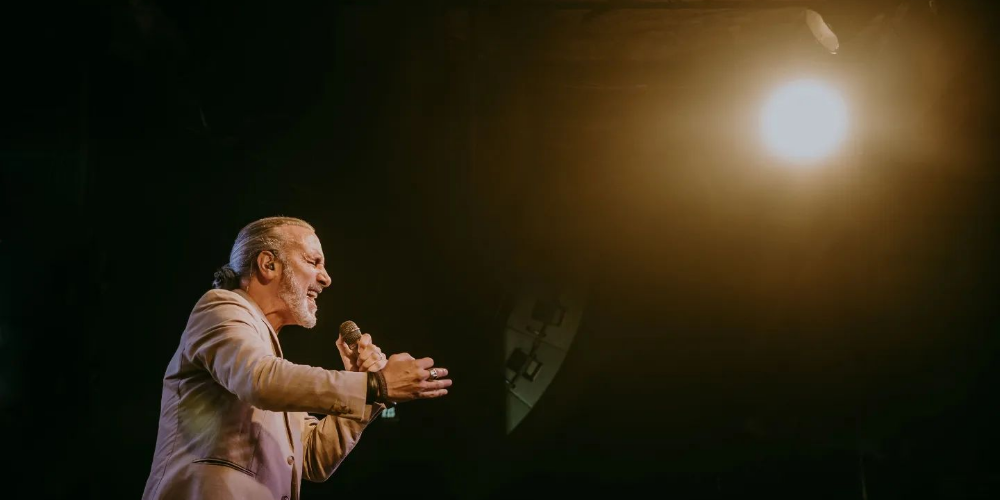 Manuel Wirzt cantando con los ojos cerrados, luciendo un traje gris y sosteniendo el micrófono