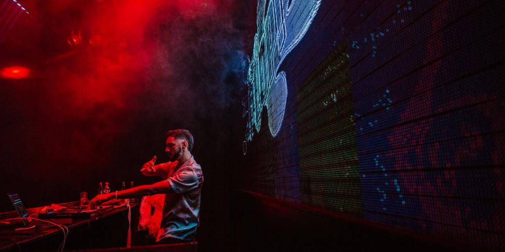 DJ animando con música vibrante en la Fiesta Plop, iluminado por luces coloridas