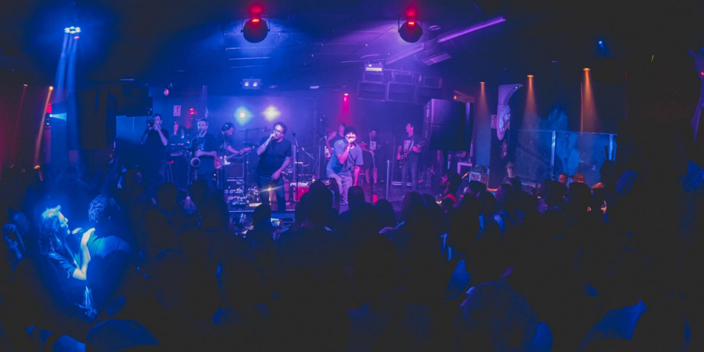 La banda de rock uruguaya La Vela Puerca se presenta en vivo en el escenario, con el público iluminado por un cautivador haz de luces azules