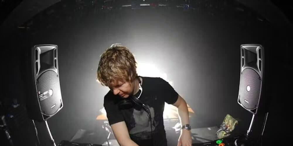 John Digweed tocando música con una remera negra, rodeado de dos potentes parlantes a cada lado