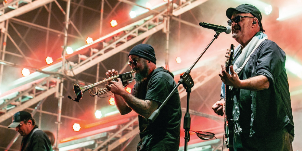 Tres integrantes de Las Pelotas tocando en concierto, entregando su característica energía en una apasionante interpretación musical