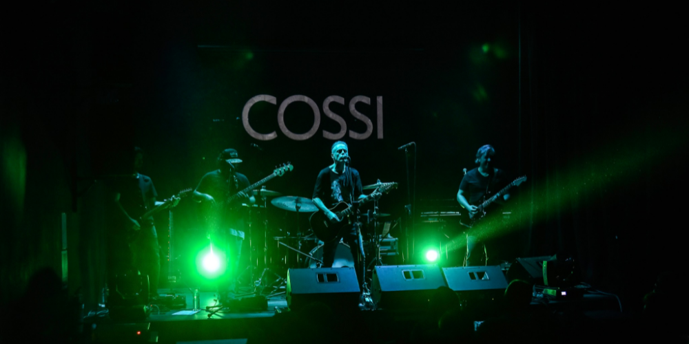 Los miembros de la banda Cossi en plena actuación en el escenario, bajo un fascinante juego de luces verdes que se proyectan hacia el público