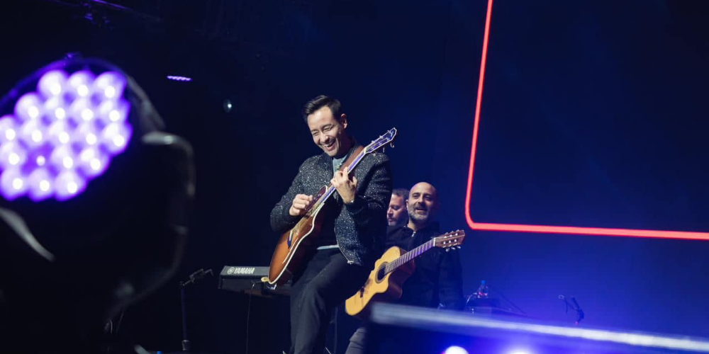 Luciano Pereyra sonriendo ampliamente mientras toca en un concierto en vivo, transmitiendo felicidad y energía positiva con su música