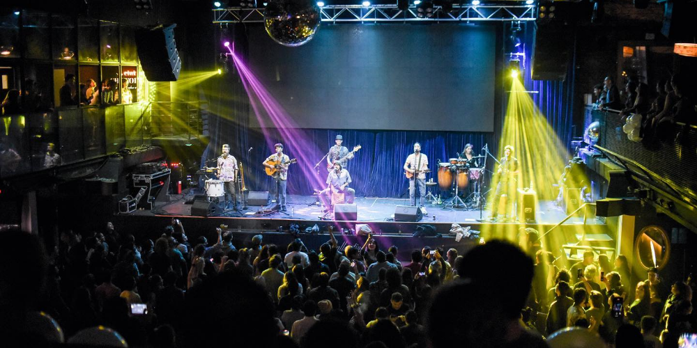 Onda Vaga tocando en vivo sobre el escenario, vista desde la perspectiva del público con la banda en plena actuación