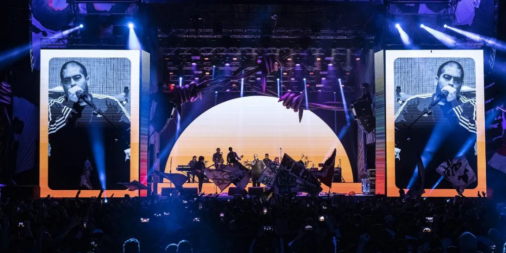 Imagen de Don Osvaldo en concierto, vista desde la perspectiva del público: la banda en pleno despliegue energético sobre el escenario iluminado, mientras una multitud de fans disfruta de la música en vivo