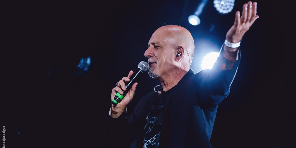 Gustavo Cordera sosteniendo un micrófono con una mano y extendiendo el otro brazo hacia un costado en un gesto apasionado durante una presentación en vivo