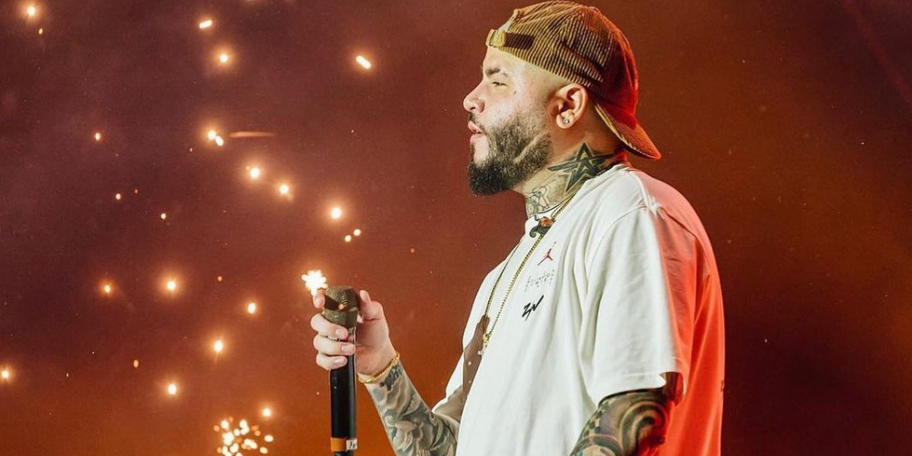 Farruko con remera blanca y gorra hacia atrás sosteniendo un micrófono, conectando con el público en un concierto