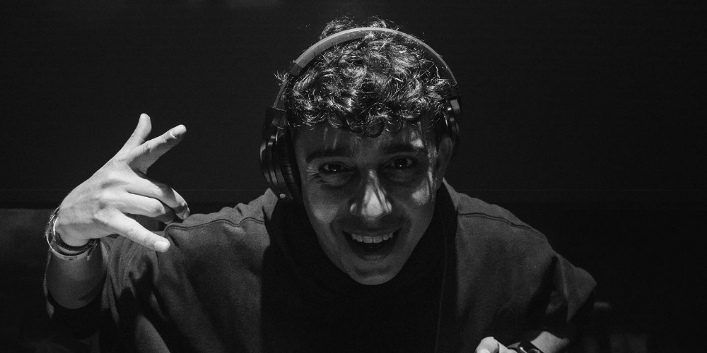 Mariano Mellino en blanco y negro sonriendo a la cámara, con auriculares de DJ y haciendo la mano cornuta