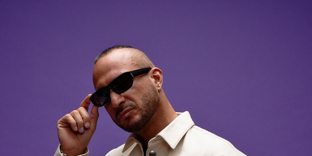 DJ Loco Dice con gafas de sol y camisa crema sobre fondo púrpura, proyectando una imagen cool y reflexiva