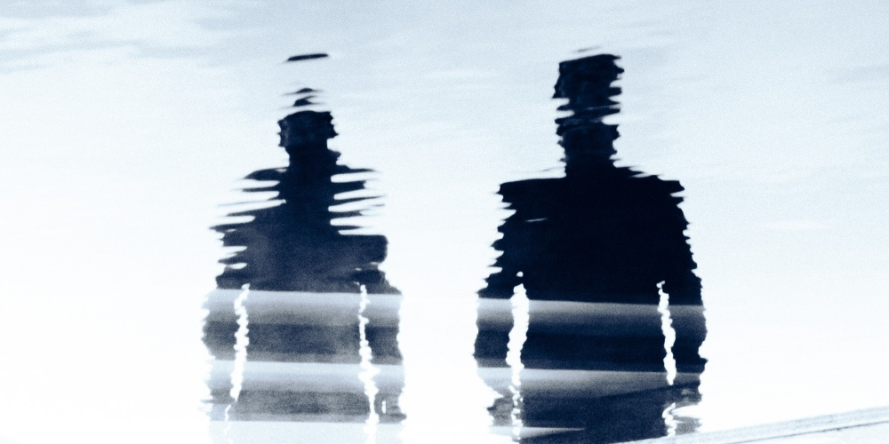 Imagen abstracta de las siluetas distorsionadas de Tale Of Us reflejadas en el agua, con una paleta de colores azul y gris que transmite una atmósfera melódica y enigmática